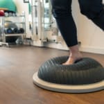 Person, die in einem Fitnessstudio auf einem runden Balancetrainer auf einem Bein balanciert.