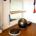 Eine Fitnessecke mit Spiegel, Widerstandsbändern, Kabelzugmaschine, Bosu-Ball, Gymnastikball, TRX-Bändern und Holzboden.