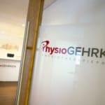 Eingang zur Physiotherapiepraxis PhysioGehrken. Im Hintergrund ist eine Glastür mit dem Logo und der Rezeption zu sehen.