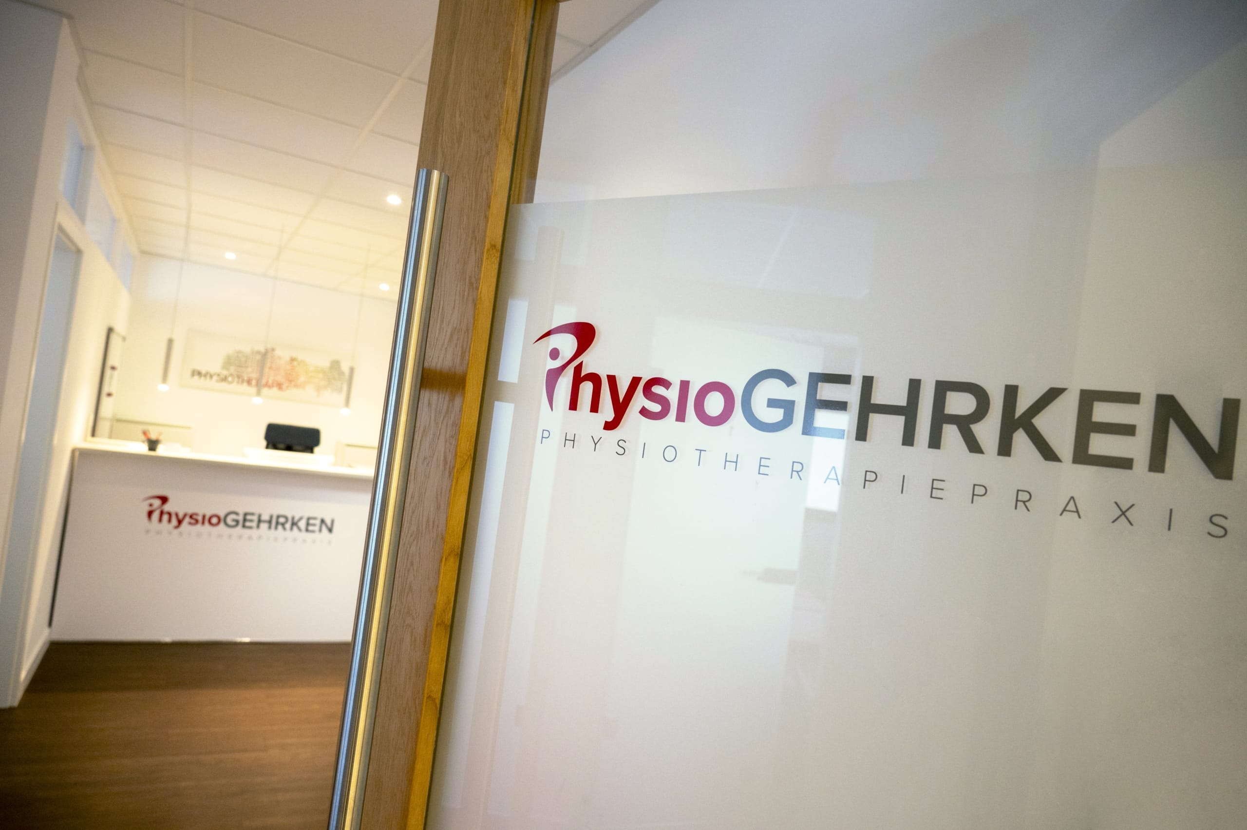 Eingang zur Physiotherapiepraxis PhysioGehrken. Im Hintergrund ist eine Glastür mit dem Logo und der Rezeption zu sehen.