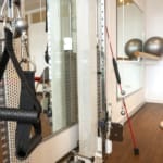 Ein Fitnessstudio mit Trainingsgeräten wie Widerstandsbändern, Balancebällen und einer Kabelmaschine in einem verspiegelten Raum.